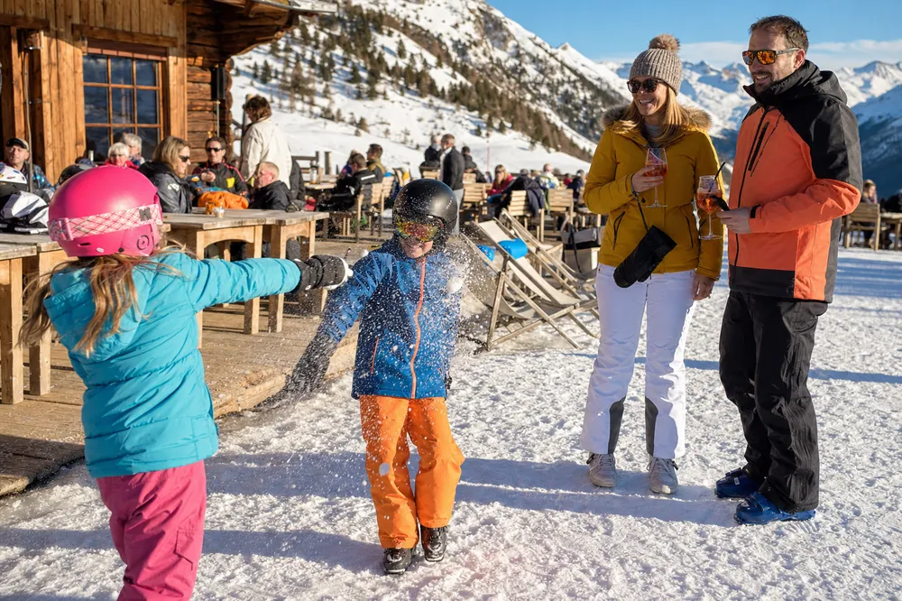 Děti v lyžařských helmách si hrají ve sněhu před horskou restaurací